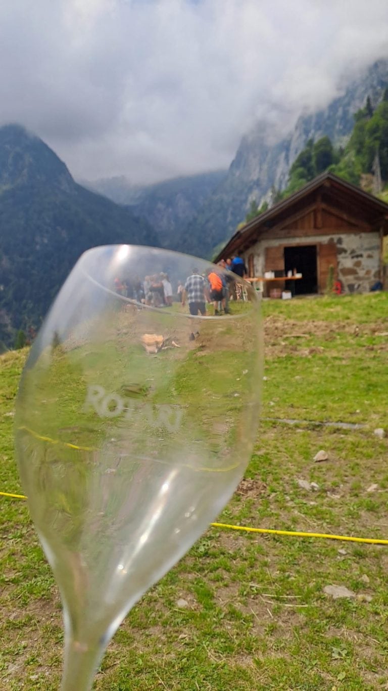 Un calice in primo piano con la malga e i partecipanti sullo sfondo